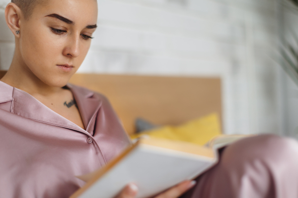 Portrait of young woman with cancer reading a book, cancer awareness concept.