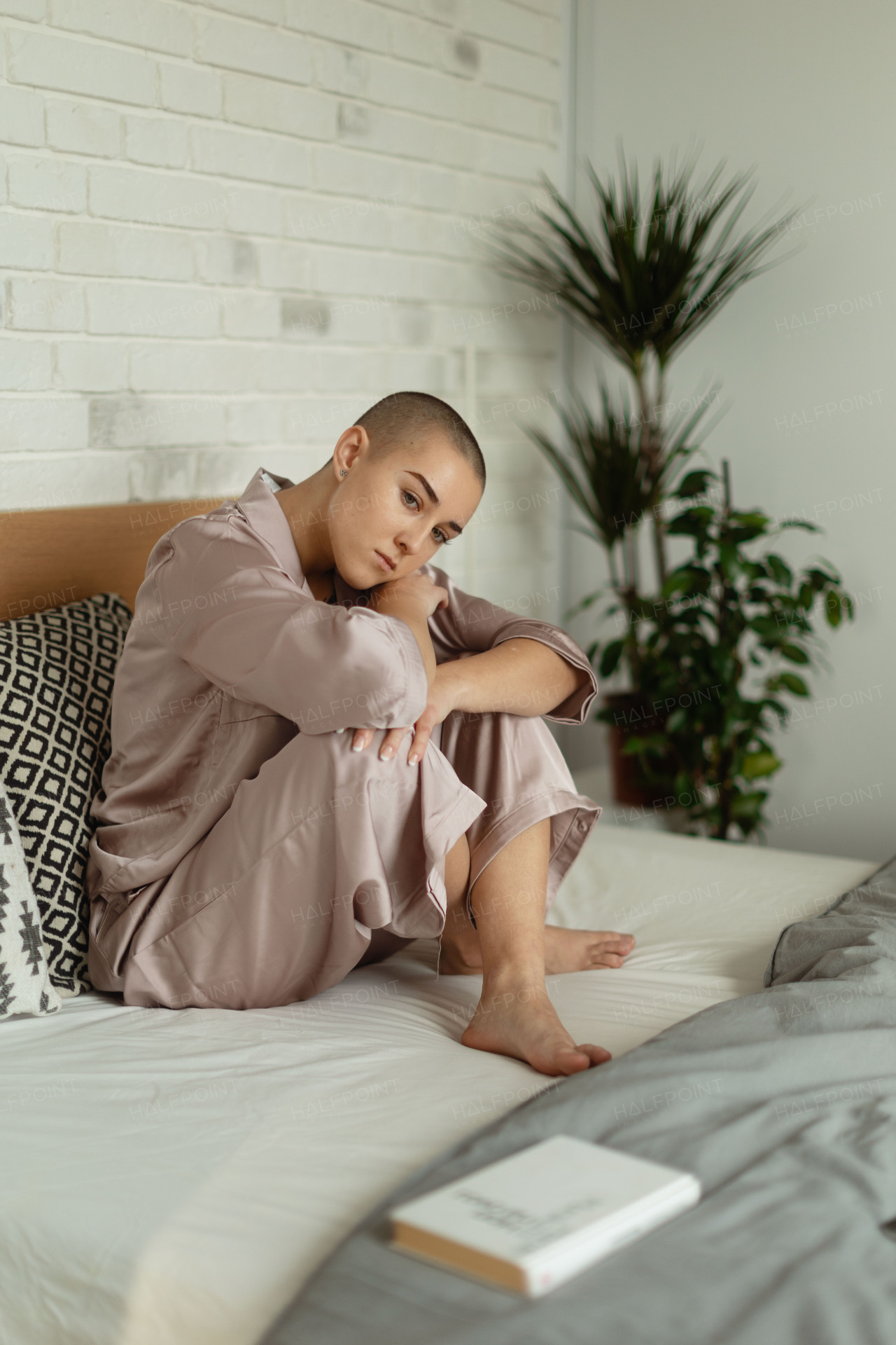 Young woman with cancer in bed with a book, cancer awareness concept.