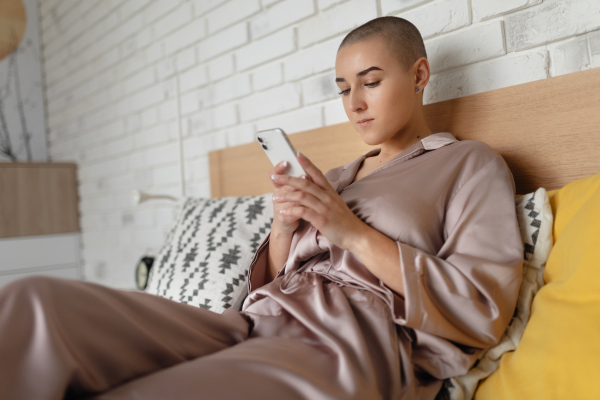 Young woman with cancer siting at home and scrolling a phone.