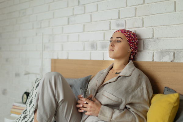 Young woman with cancer drinking water and lying in a bed, cancer awareness concept.