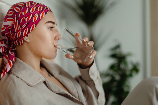 Portrait of young woman with cancer drinking water and lying in a bed, cancer awareness concept.