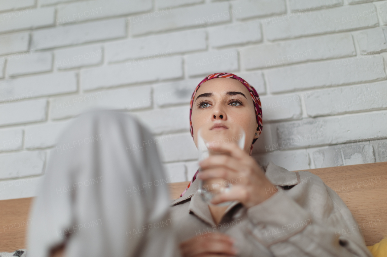 Young woman with cancer drinking water and lying in a bed, cancer awareness concept.