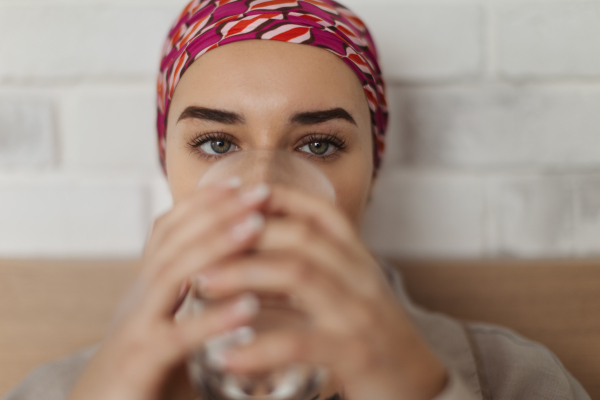 Portrait of young woman with cancer drinking water and lying in a bed, cancer awareness concept.