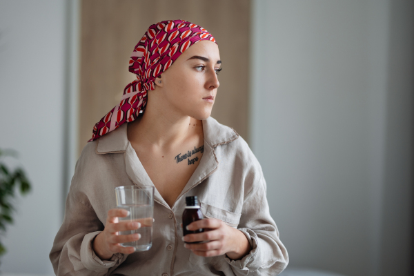 Young woman with cancer taking the pills, cancer awareness concept.