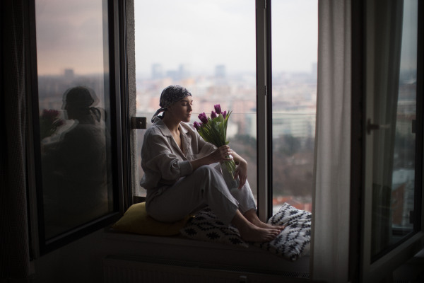 Young woman with cancer sitting in a window and smelling bouquet of tulips.