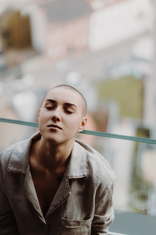 High angle view of young unhappy woman with cancer sitting in window.