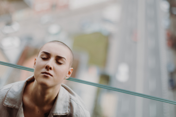 High angle view of young unhappy woman with cancer sitting in window.