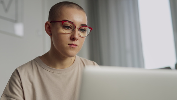 Young woman with cancer working on laptop in the apartment.