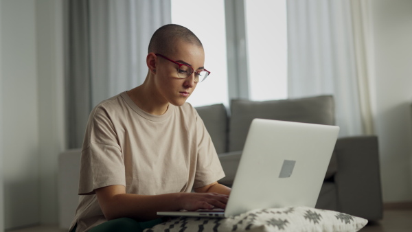 Young woman with cancer working on laptop in the apartment.