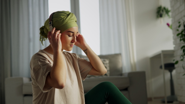 Young woman with cancer siting at home and scrolling a phone and listening the music.