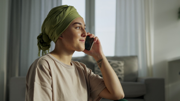 Young woman with cancer siting at home and scrolling a phone.