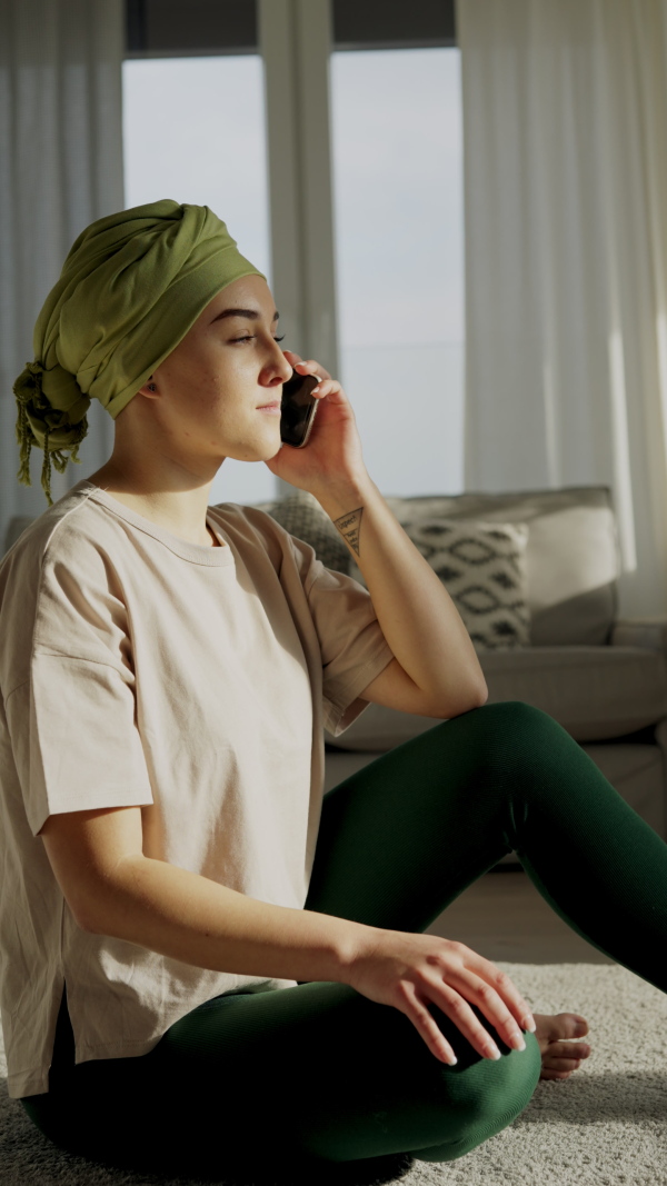 Young woman with cancer siting at home and scrolling a phone. Vertical footage.