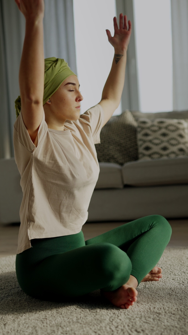 Young woman with cancer taking yoga and meditating in the apartment. Vertical footage.