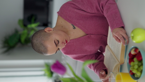 Young woman with cancer reading a book, cancer awareness concept. Vertical footage.