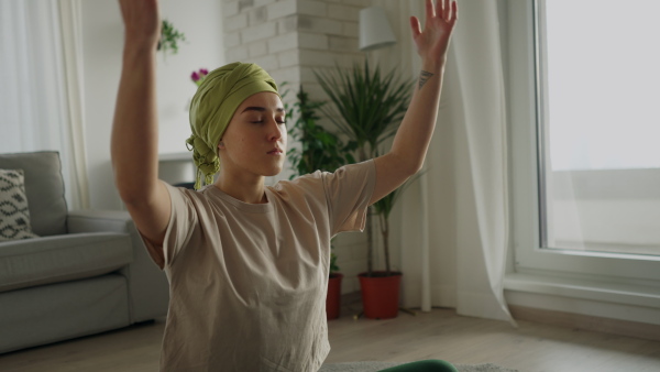 Young woman with cancer taking yoga and meditating in the apartment.