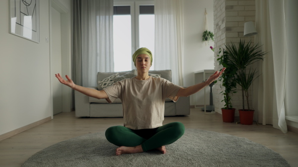 Young woman with cancer taking yoga and meditating in the apartment.