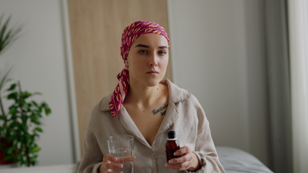 Young woman with cancer taking the medicine, looking at camera., cancer awareness concept.