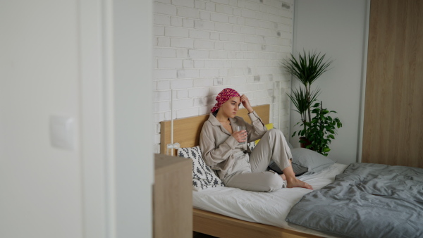 A young woman with cancer drinking water and lying in a bed, cancer awareness concept.