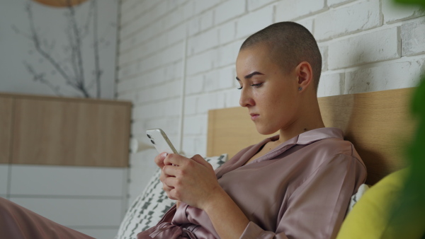 Young woman with cancer siting at home and scrolling a phone.