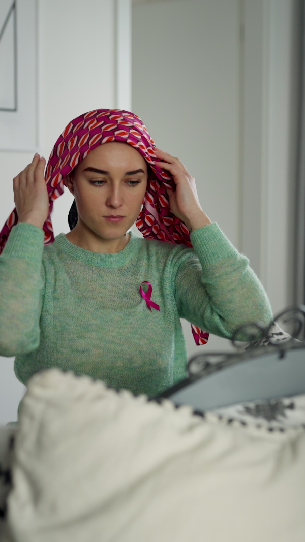 Beauty routine of a young woman with cancer, getting scarf on her head. Vertical footage.