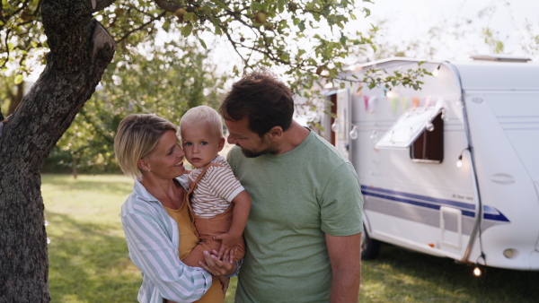 Family with small toddler traveling in caravan, camping and exploring new places. Mother holding boy in arms, smiling.