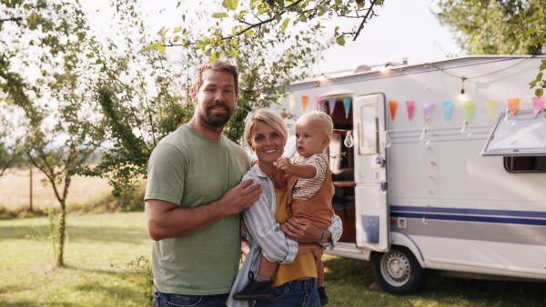 Family with small toddler traveling in caravan, camping and exploring new places. Mother holding boy in arms, smiling.