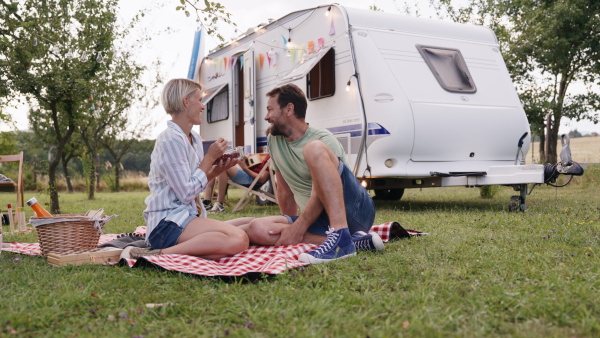 Family traveling in a caravan, camping and exploring new places. Parents sitting on blanket eating grapes, having picnic.