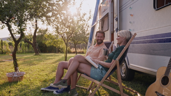 Family traveling in caravan, camping and exploring new places. Parents sitting in front of a caravan, relaxing during sunset.