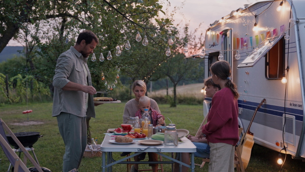 Family traveling in a caravan, having picnic diner. Parents with three kids during camping trip.