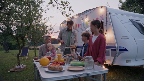 Family traveling in a caravan, having picnic diner. Parents with three kids during camping trip.