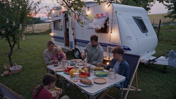 Family traveling in a caravan, having picnic diner. Parents with three kids during camping trip.