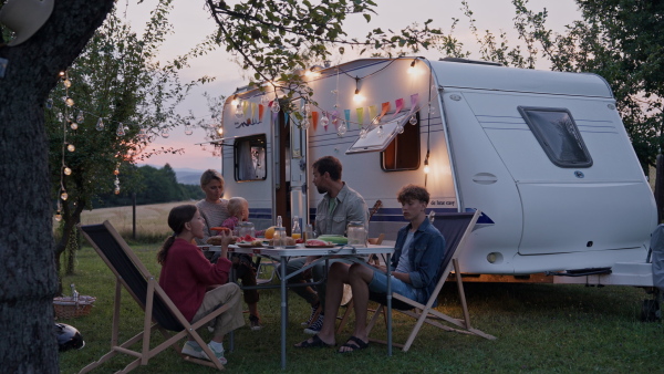 Family traveling in a caravan, having picnic diner. Parents with three kids during camping trip.