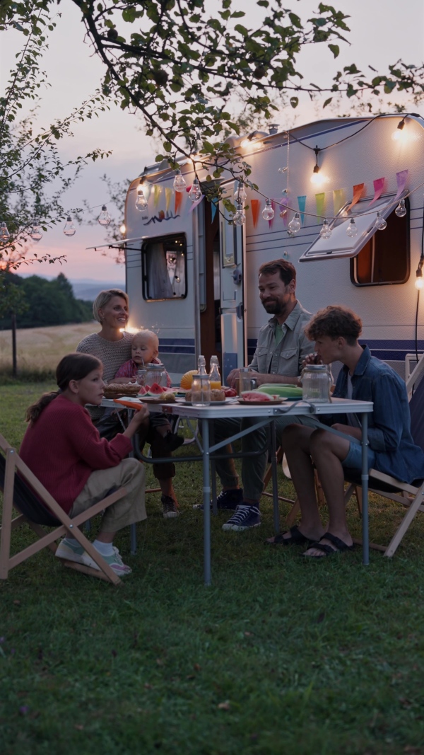 Family traveling in a caravan, having picnic diner. Parents with three kids during camping trip.