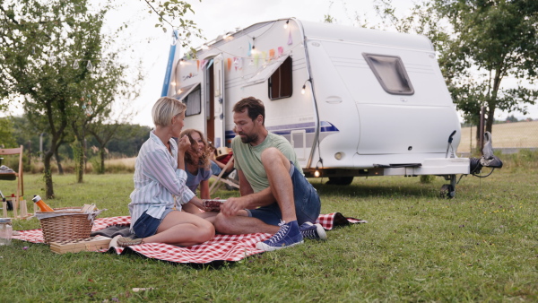 Family traveling in a caravan, camping and exploring new places. Parents sitting on blanket eating grapes, having picnic.