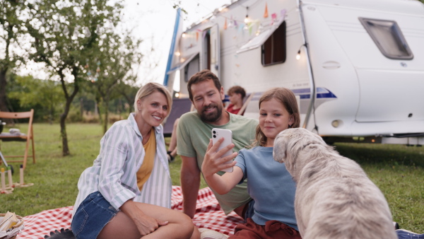 Family traveling in a caravan, camping and exploring new places. Parents and girl taking selfie with smartphone, making video call.