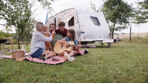 Family traveling in a caravan, exploring new places. Parents with three kids having picnic in front of caravan, sitting on blanket.