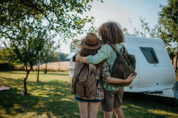 Rear view of couple looking at caravan. Young man and woman on camping trip in nature traveling in camper.