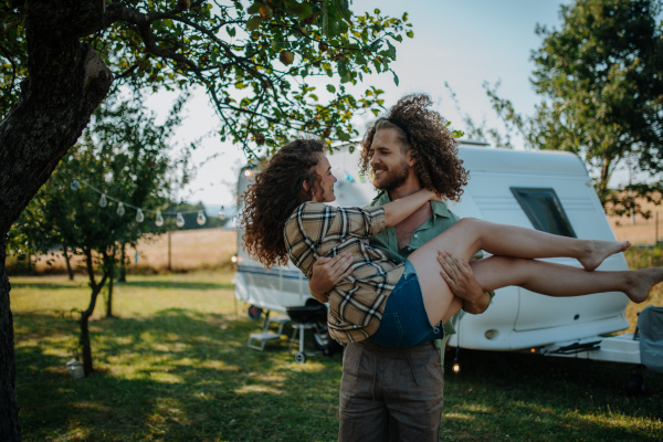 Man in love holding his fiancee in arms. Young couple is on a camping trip in nature traveling by caravan