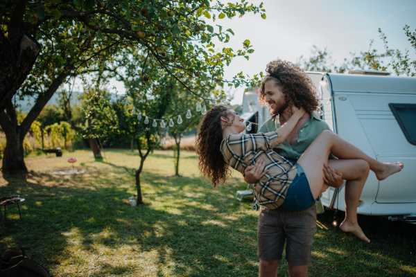 Man in love holding his fiancee in arms. Young couple is on a camping trip in nature traveling by caravan