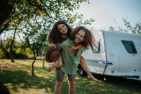 Man in love piggibacking his girlfriend. Young couple is on a camping trip in nature traveling by caravan