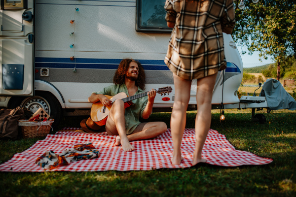 Couple sitting by caravan, enjoying peaceful moment. Man playing guitar and singing song to his girlfriend.