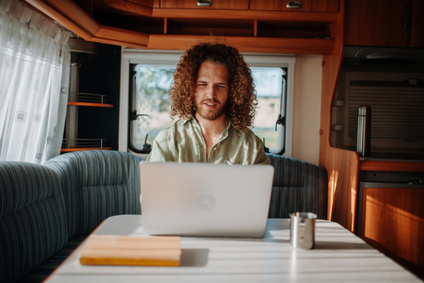 Young man working remotely from caravan. Man using camper as homeoffice, working on notebook