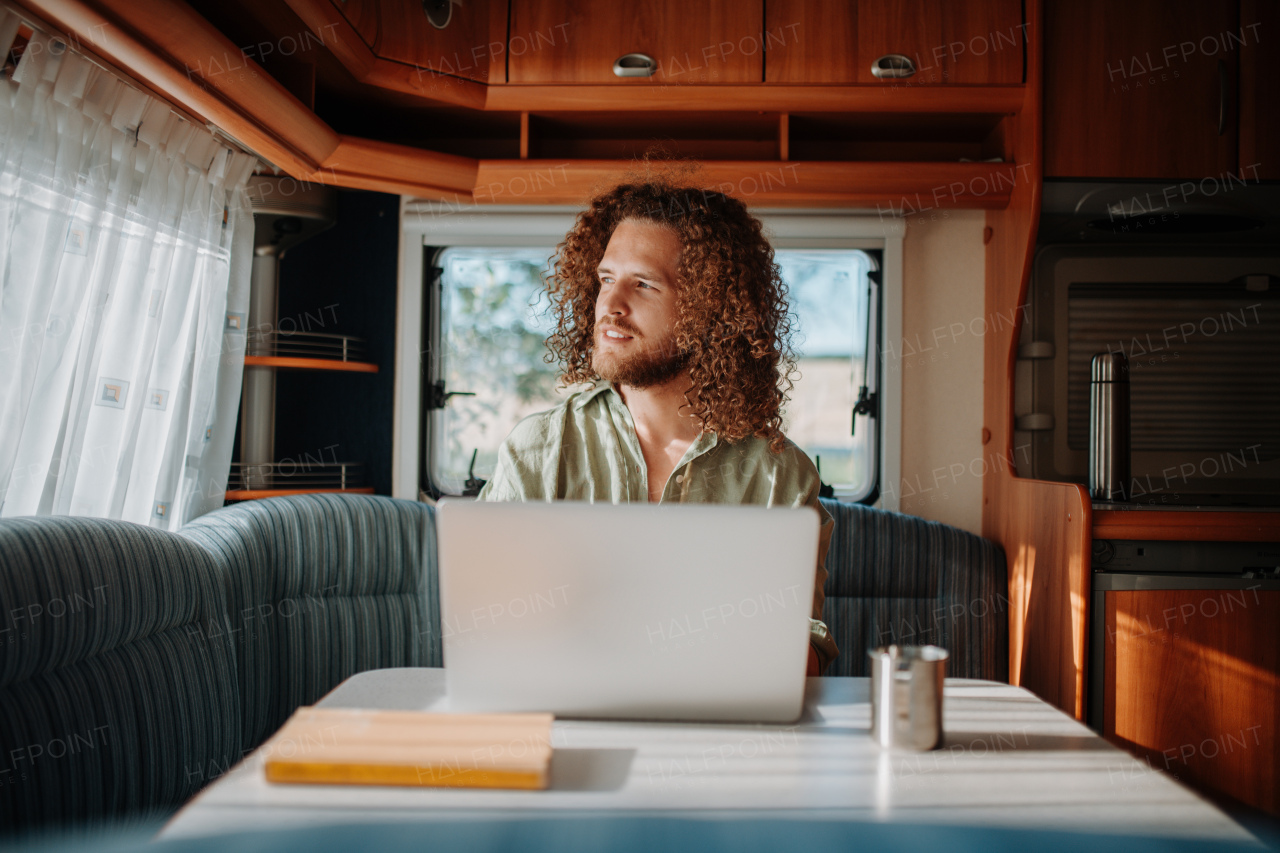 Young man working remotely from caravan. Man using camper as homeoffice, working on notebook