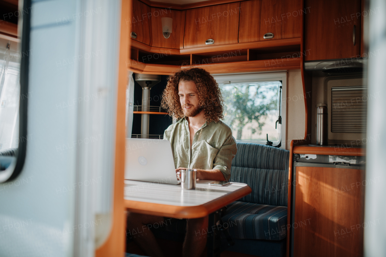 Young man working remotely from caravan. Man using camper as homeoffice, working on notebook