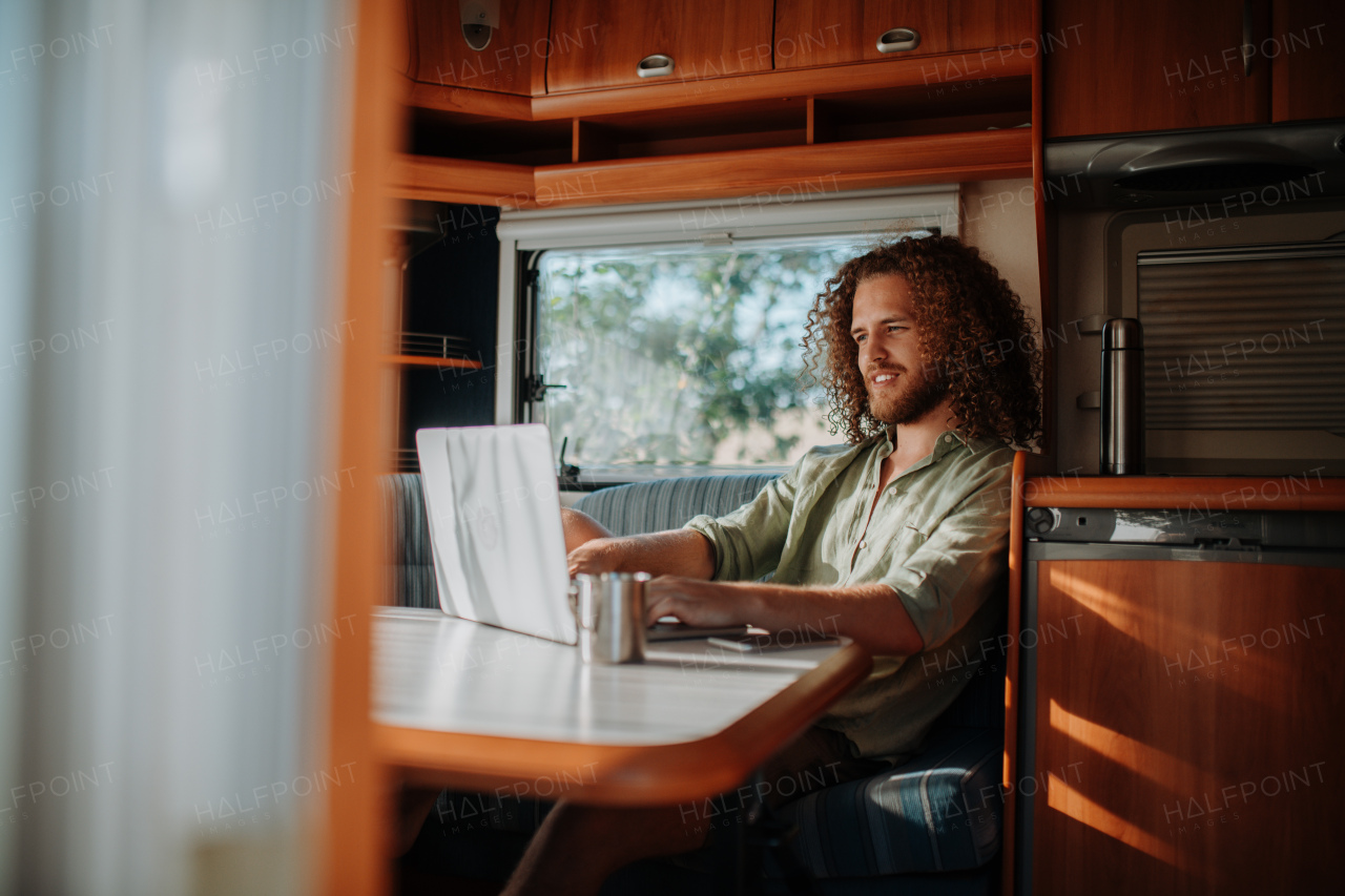 Young man working remotely from caravan. Man using camper as homeoffice, working on notebook