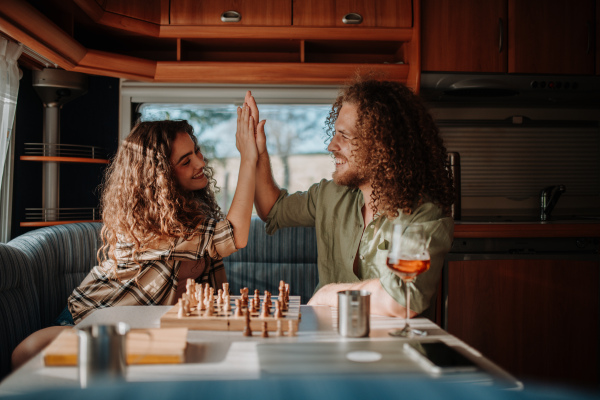 Young couple is on a camping trip in nature, sitting in caravan and playing chess.