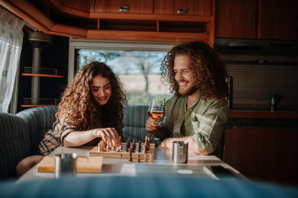 Young couple is on a camping trip in nature, sitting in caravan and playing chess.