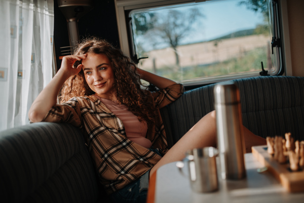 Young beautiful woman is on a camping trip in nature, sitting in her caravan and enjoying morning cup of coffee