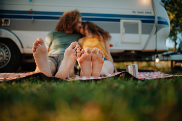 Couple sitting by caravan and kissing, enjoying a cup of morning coffee outdoors. Camping trip for young people.