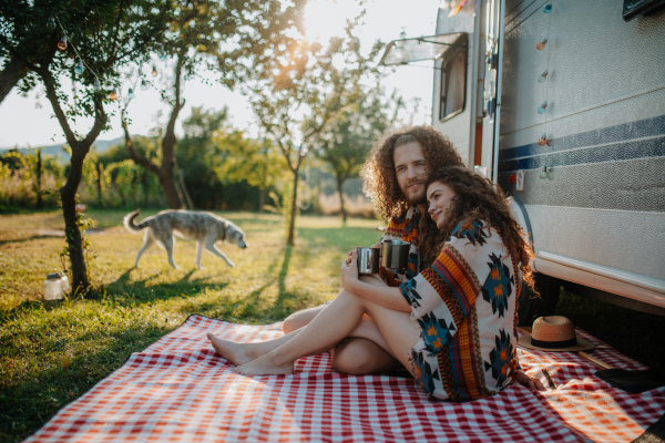 Couple sitting by caravan, enjoying peaceful moment, drinking coffee of herbal tea.